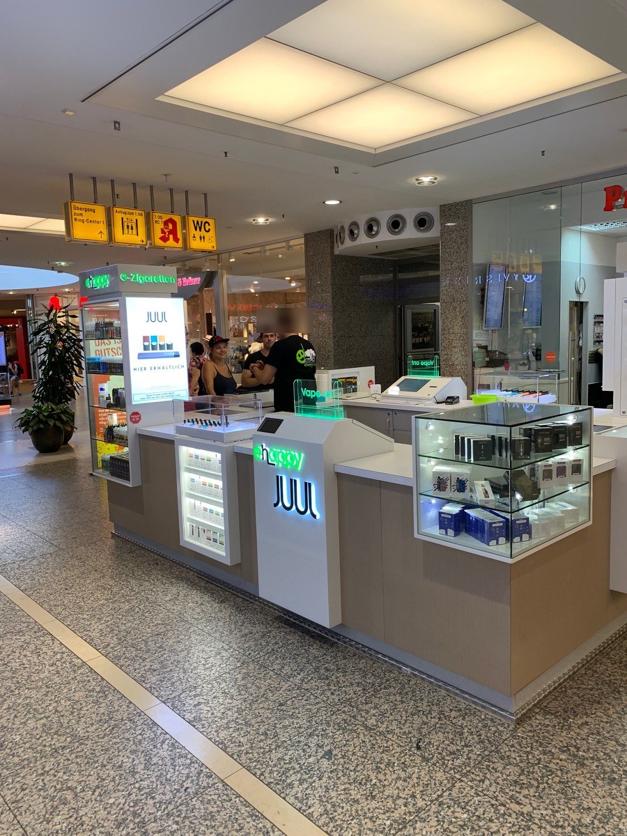 Verkaufsinsel mit weißer Theke, Glasvitrinen und beleuchteten Aufsätzen in einer Mall